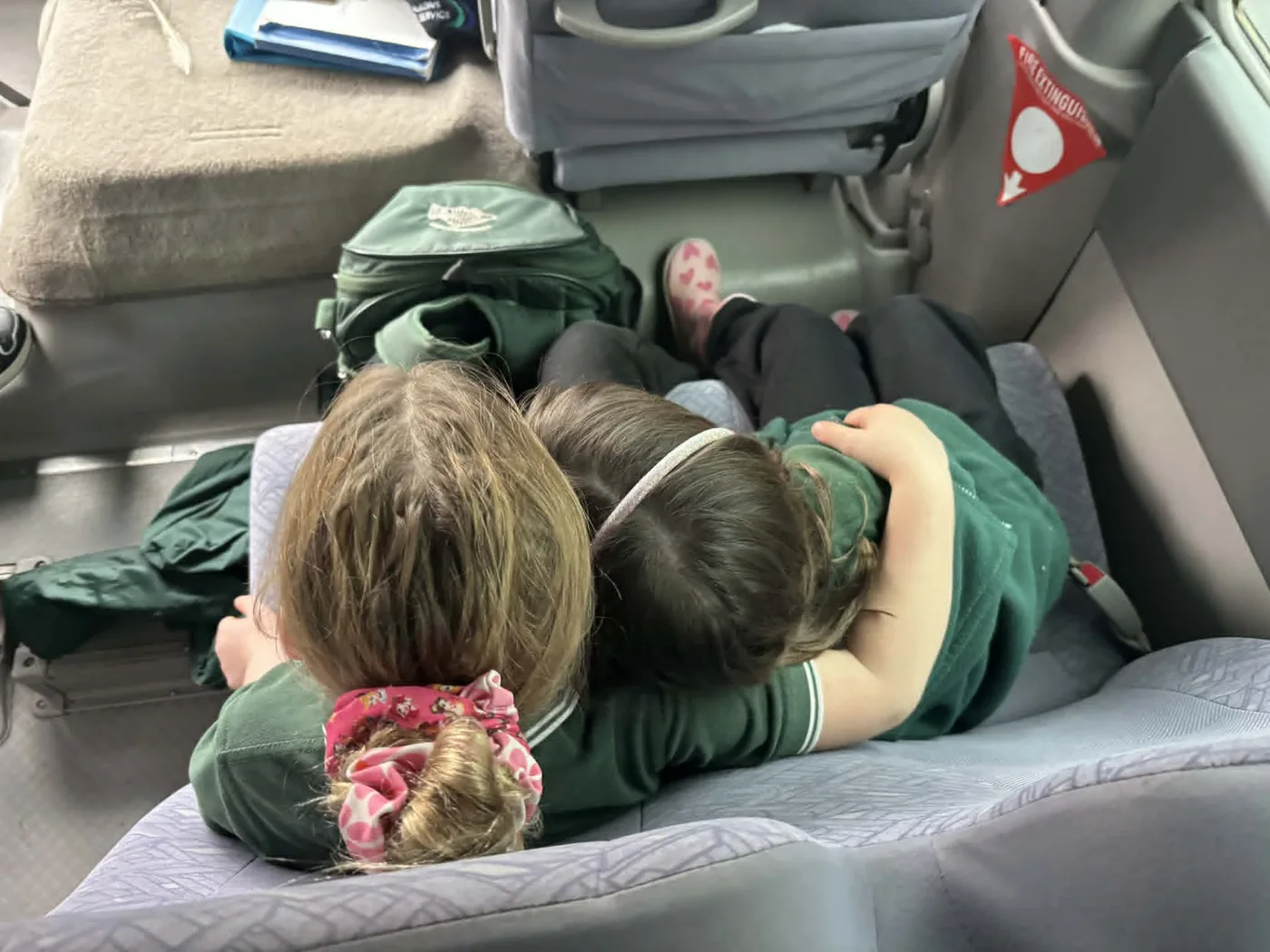Two Carra students resting together on the school bus, a green Carra backpack beside them