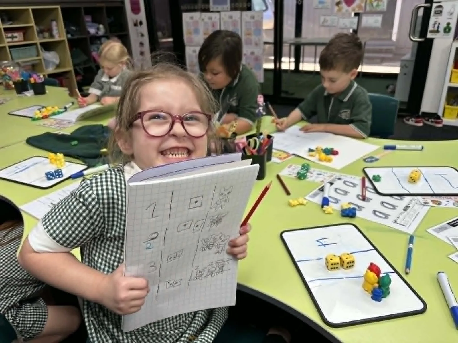A Foundation student smiling while holding her maths workbook during a hands-on lesson at Carra