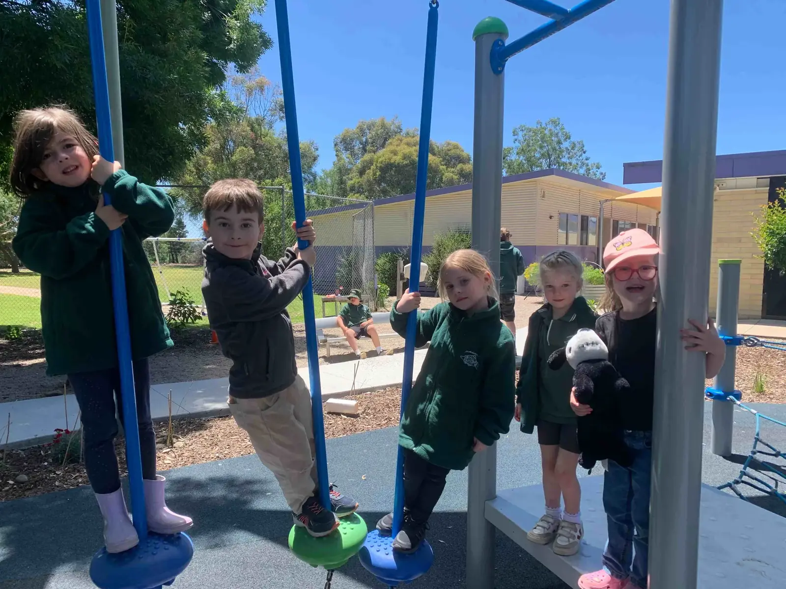 Carraragarmungee Primary School students playing together on the outdoor playground equipment on a sunny day, with the school buildings and gum trees behind